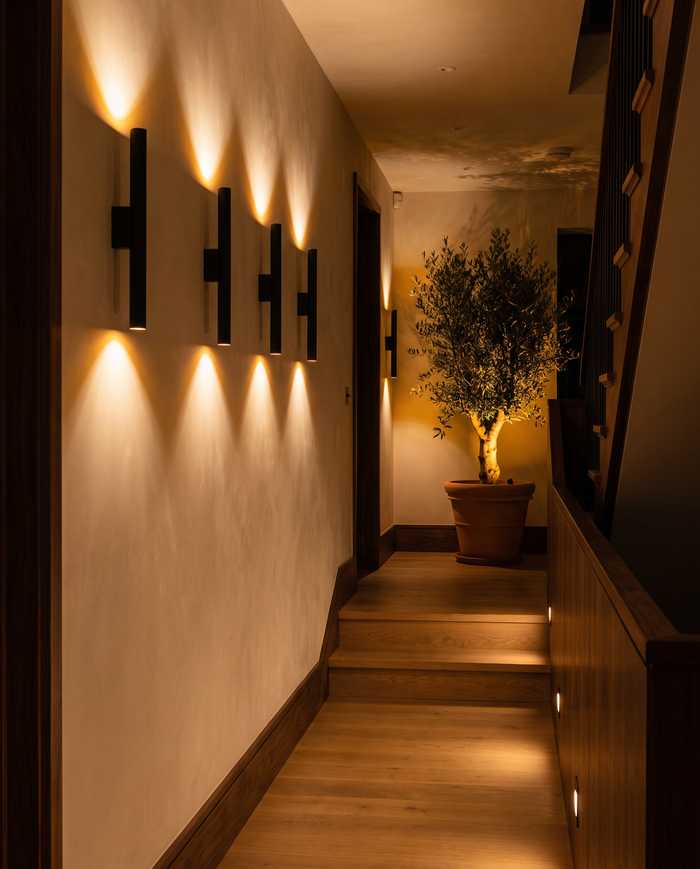 Row of matte black LED wall sconces washing warm light up a cream plaster hallway wall