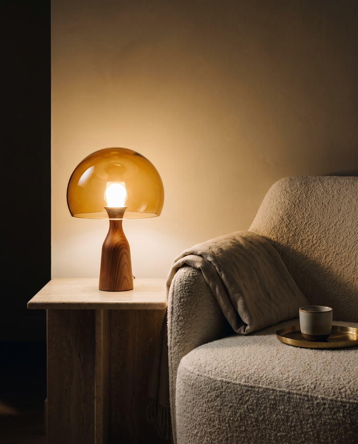 Amber glass and walnut table lamp glowing on a travertine side table at night
